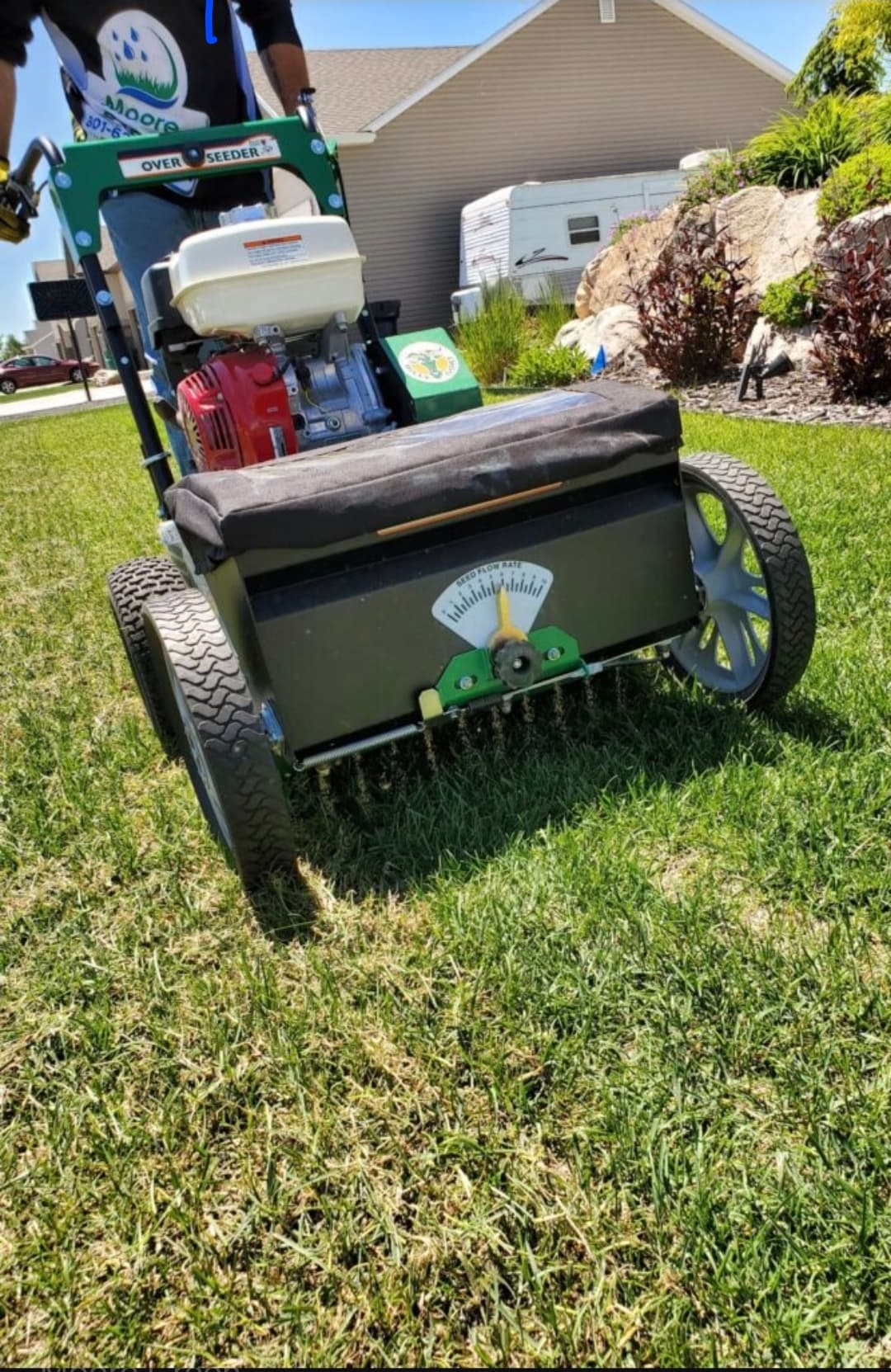 Motorized overseeder machine with a Honda engine being used on a green residential lawn.